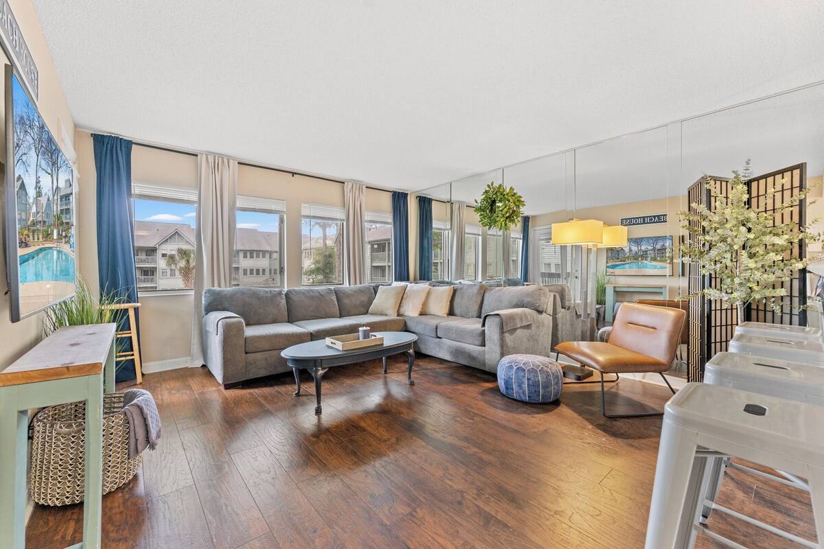 A modern living room with a sectional sofa, a coffee table, and a view of a pool and buildings.
