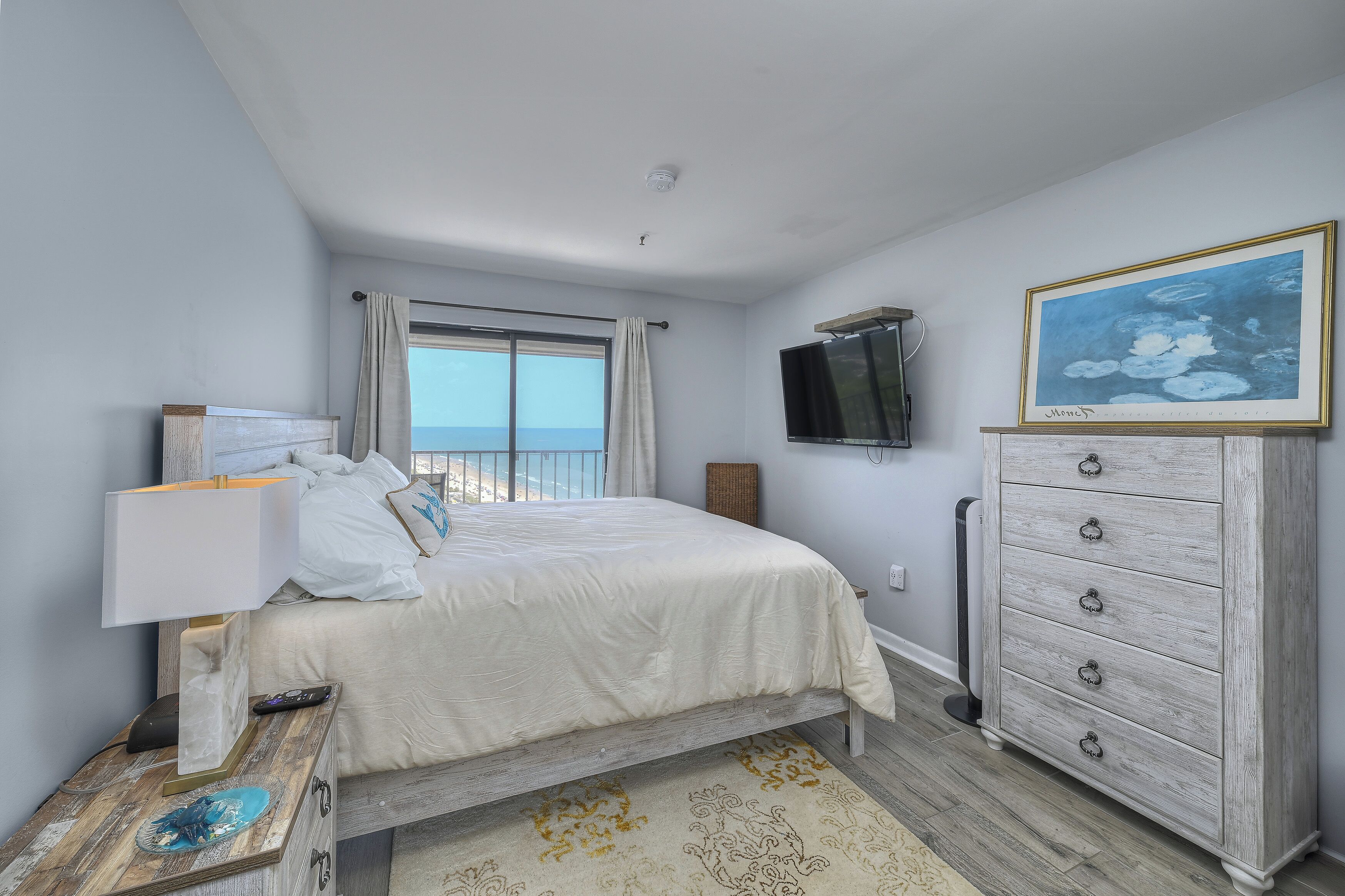 A bedroom with a bed, bedside table, dresser, TV, and a window with curtains.