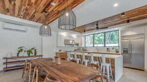 Une cuisine moderne avec un plafond en bois, un grand îlot central doté de tabourets de bar et un réfrigérateur en acier inoxydable.