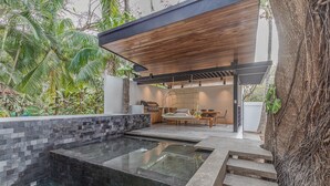 Un espace piscine extérieur moderne, agrémenté d’un mur en pierre, d’une pergola en bois et d’un coin salon avec une chaise et une table.