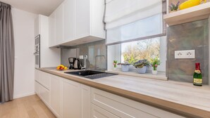 A modern kitchen with white cabinets, a black sink, and a window with potted plants. - Luxury Villa Confidenza with Pool (Malinska)