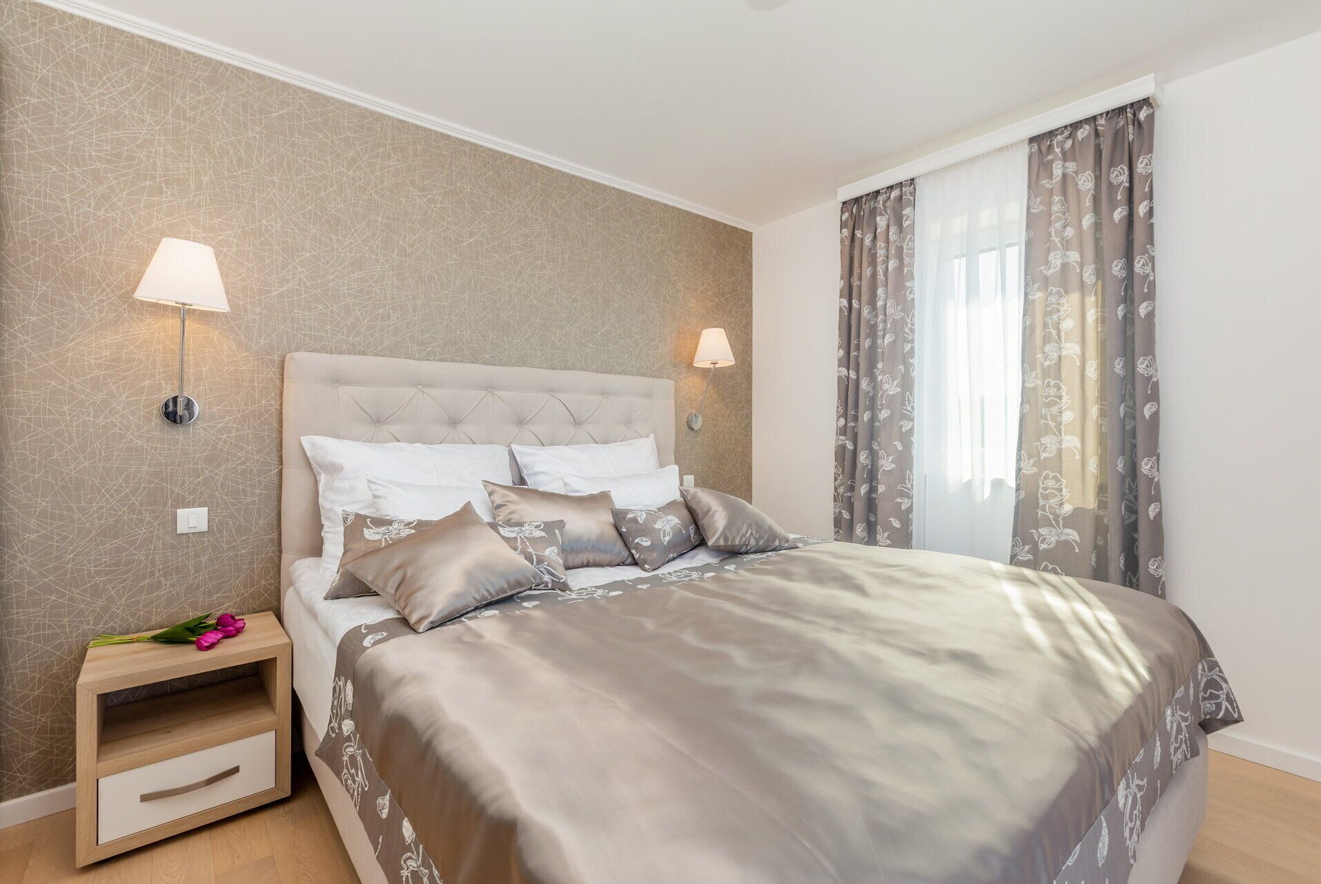 A bedroom with a tufted headboard, a bedside table with a lamp, and a window with curtains.