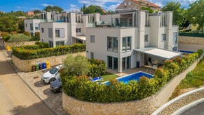 A modern multi-story residential building with a rooftop pool, surrounded by lush greenery and stone walls.