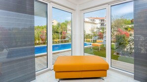 A modern room with large windows, a pool, and outdoor seating.