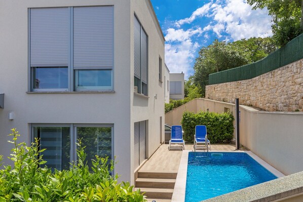 A modern building with a swimming pool, blue lounge chairs, and a stone wall. - Villa Sapphire with Heated Pool (Malinska)
