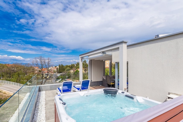 Un espace piscine aménagé sur le toit, avec un jacuzzi, des chaises longues et une balustrade en verre donnant sur un panorama urbain.
