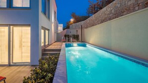 Un área de piscina moderna con una piscina azul cristalina, un muro de piedra y una cubierta de madera.