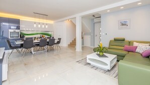 Una sala de estar moderna con un sofá verde, una mesa de centro blanca y un comedor con una mesa y sillas blancas.