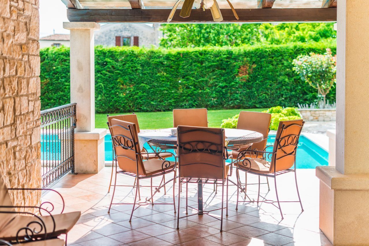 Een terras met een ronde tafel en stoelen, een zwembad en uitzicht op een verzorgde tuin.