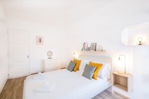 A neatly arranged bedroom with a large bed, bedside tables, and a wall-mounted shelf with decorative items.