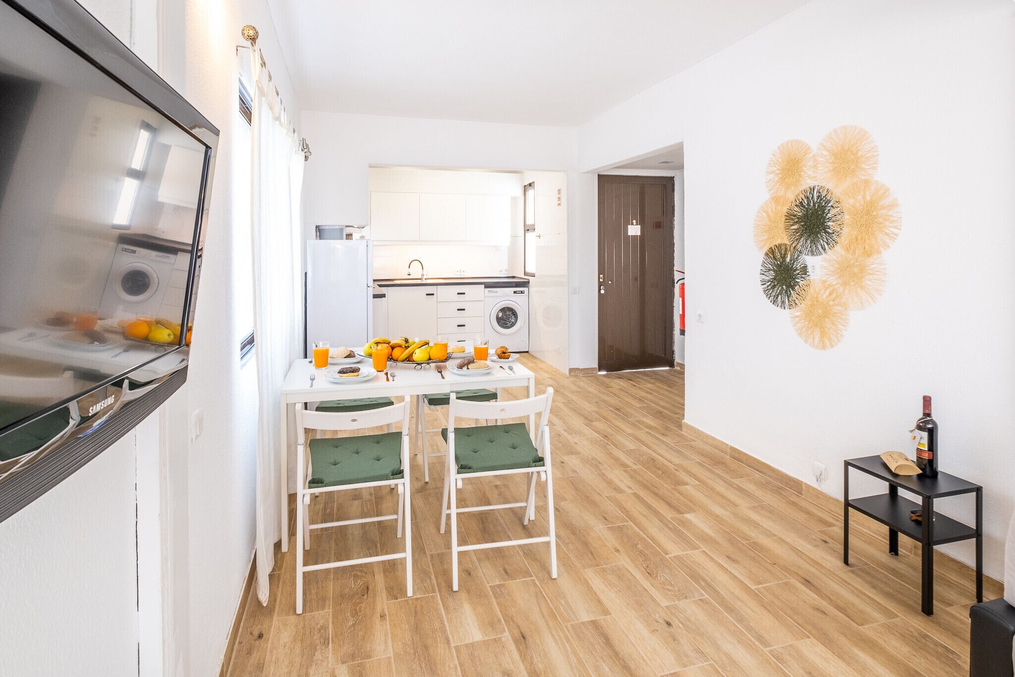A compact kitchen with a dining area, a washing machine, and a small table with a bottle of wine.