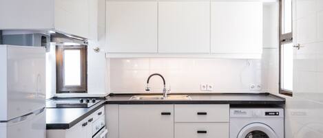 A compact kitchen with white cabinets, a stainless steel sink, a built-in washing machine, and a refrigerator.