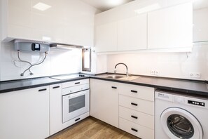 A modern kitchen with white cabinets, a built-in oven, a washing machine, and a sink.