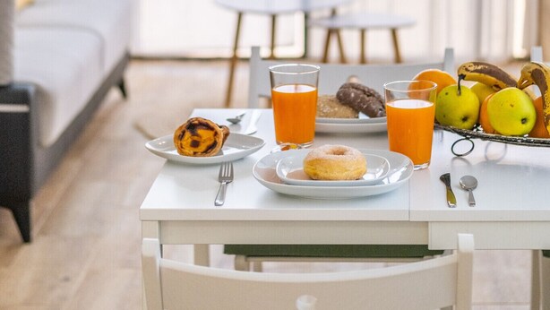 Una mesa de desayuno con platos de comida, vasos de jugo de naranja y una cesta de frutas.