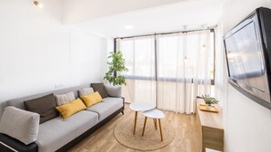 Una sala de estar moderna con un sofá, dos mesitas, una planta en maceta y un televisor montado en la pared.