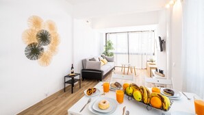 Una habitación moderna y luminosa con una mesa de comedor preparada para el desayuno, con frutas, bollería y bebidas.