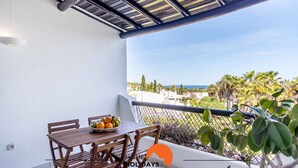 A balcony with a table and chairs, a bowl of fruit, and a view of palm trees and buildings. - #088 T2 São Rafael 64B by Home Holidays (Albufeira)