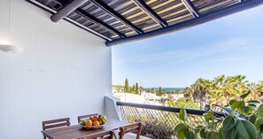A balcony with a table and chairs, a bowl of fruit, and a view of palm trees and buildings.