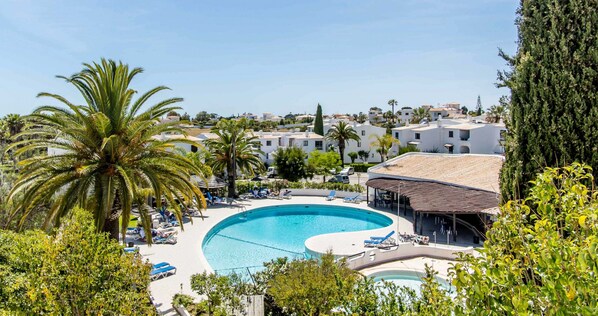 A resort with a large swimming pool surrounded by lounge chairs and palm trees.