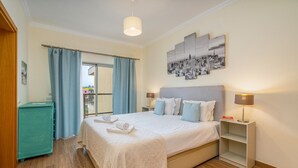 Une chambre d’hôtel avec un lit, une table de chevet, une lampe, une fenêtre avec des rideaux et un tableau représentant un paysage urbain accroché au mur.