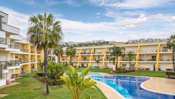 Un hôtel doté d’une piscine entourée de palmiers et d’une pelouse bien entretenue.