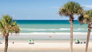 Ein Strand mit Palmen, klarem, blauem Wasser und einigen Sonnenschirmen.
