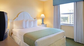 A hotel room with a bed, a nightstand, a lamp, and a view of a building through the window.