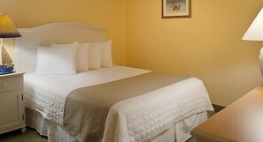 A neatly made bed with white bedding in a room with yellow walls.