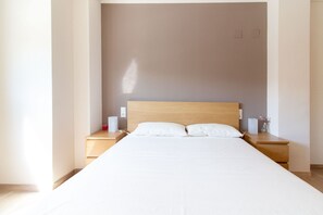 A hotel room with a large bed, wooden headboard, two bedside tables with lamps, and a neutral-colored wall.