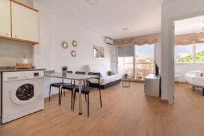 A compact living space with a kitchenette, a dining area, a bedroom, and a balcony with a view.