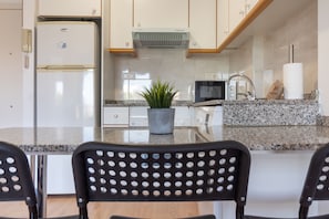 A modern kitchen with a refrigerator, microwave, stove, and granite countertop.