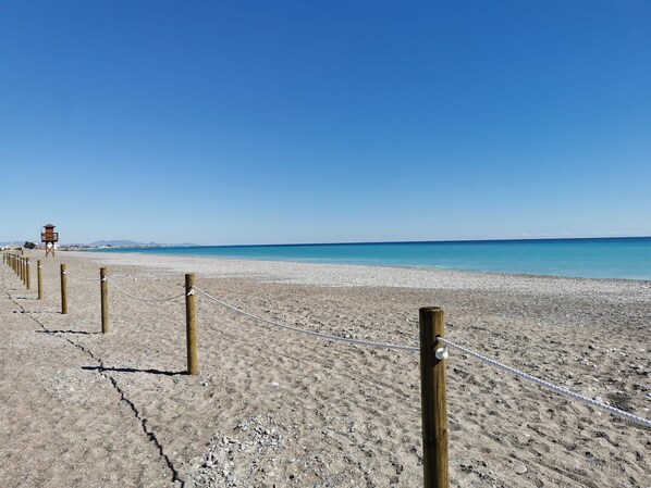 Une plage avec une tour de surveillance en contrebas, des poteaux en bois et une barrière faite de cordes.