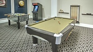 Une table de billard, une table de baby-foot et une autre table de billard se trouvent dans une pièce dont le sol est recouvert d’un tapis à motifs.