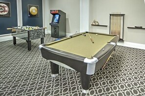 Una mesa de billar junto con una mesa de fútbol de mesa y otra mesa de billar en una sala con alfombra estampada.