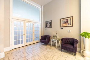 A spacious room with a large sliding glass door leading to a balcony, two armchairs, a small table with decorative items, and framed pictures on the wall.