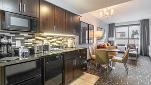 A modern kitchen with dark wood cabinets, a black countertop, and a built-in microwave. There is a dining area with a table and chairs, and a large window with curtains.