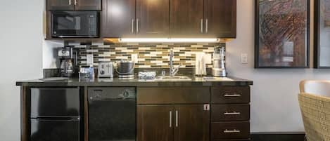 A modern kitchen with dark wood cabinets, a black refrigerator, a microwave, and a tiled backsplash.