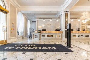 Een hotel lobby met een receptiebalie, een 'CLUB WYNDHAM' mat en een moderne kroonluchter.