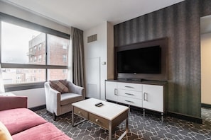 Habitación de hotel con una ventana grande, televisor de pantalla plana, sofá, mesa de centro y un armario.