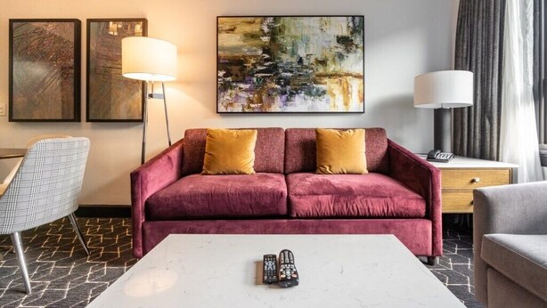 A hotel room with a red sofa, two lamps, a coffee table, and two remote controls.