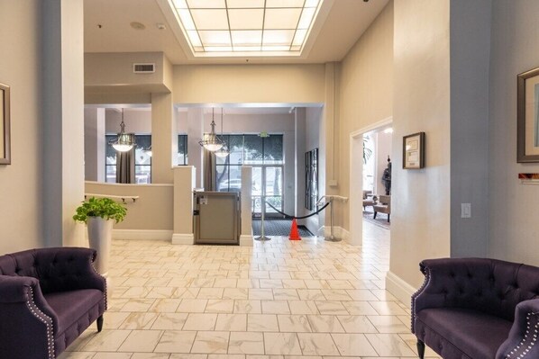 A hotel lobby with a marble floor, two purple armchairs, a reception desk, and a glass door leading to another room.