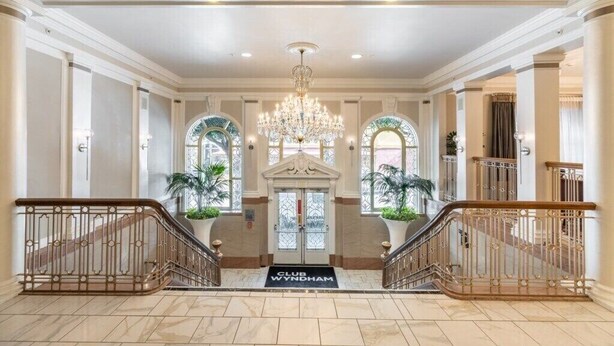Une entrée imposante, ornée d’un lustre, d’un escalier et d’un tapis portant l’inscription « CLUB WYNDHAM ».