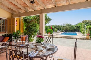 An outdoor patio with a table set for dining, a pool, and lush greenery.