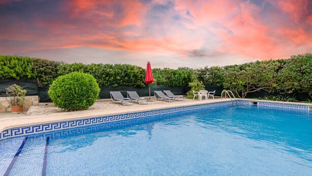 Une piscine agrémentée d’un bord décoratif, de chaises longues et d’un parasol rouge.