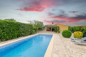 A swimming pool with a tiled edge, a stone patio, and a small building in the background.