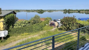 Uitzicht op een meer met een huis, geparkeerde auto's en een metalen hekwerk.