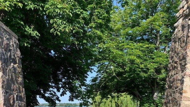 Een pad van stenen dat naar een waterpartij leidt, omringd door bomen en een stenen muur.