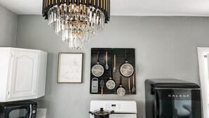 Une cuisine équipée d’un four à micro-ondes blanc, d’une cuisinière, d’une machine à café Galanz, d’un lustre et d’un panneau perforé sur lequel sont accrochés des ustensiles de cuisine.