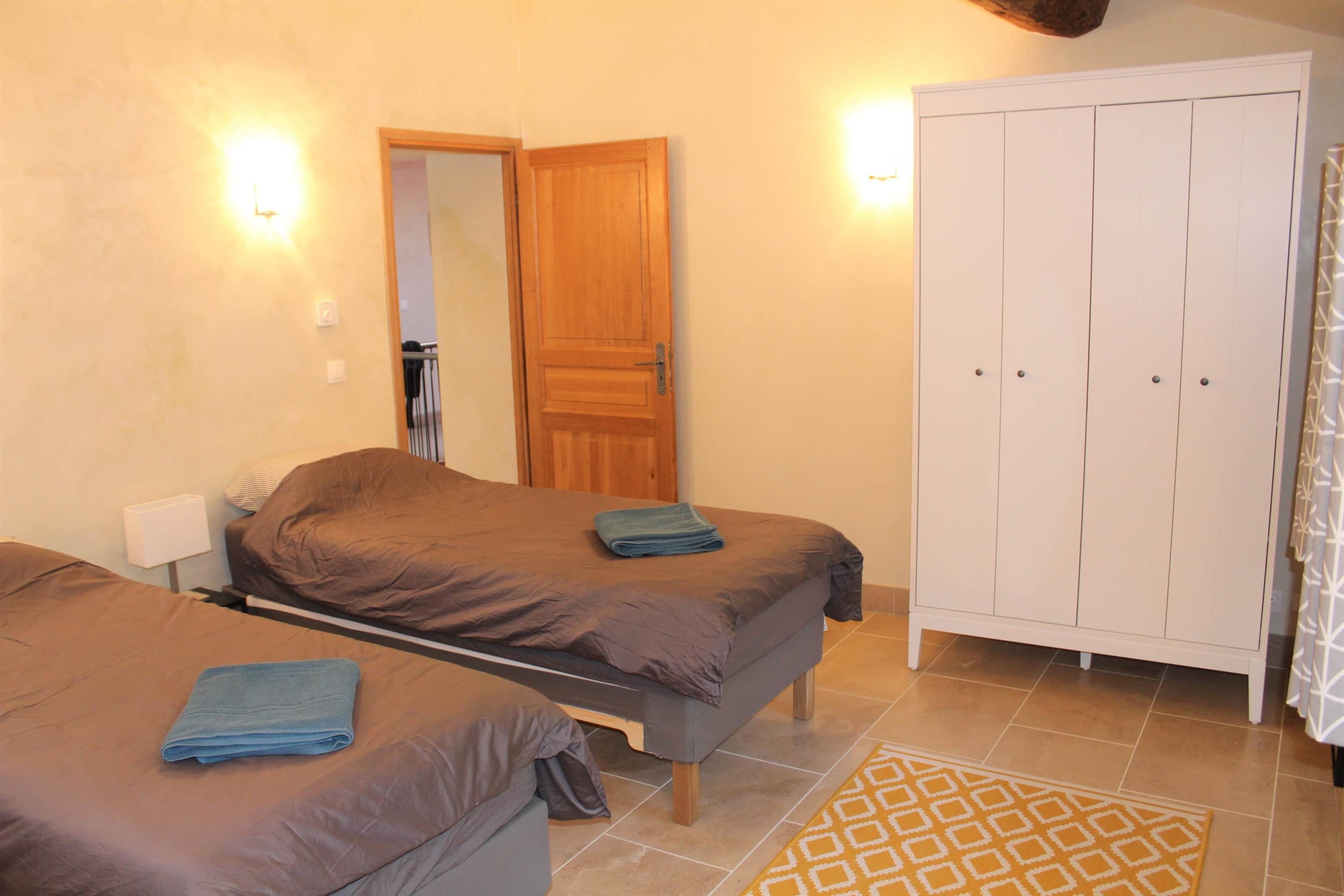 Una camera da letto con due letti, un armadio e un bagno visibile attraverso una porta aperta.