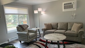 Een woonkamer met een gestreept fauteuil, een beige bank, een ronde salontafel en een vloerkleed met een patroon.
